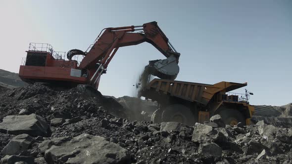 Excavator Lifts Bucket Filled with Coal and Pours It Into Mining Truck alt