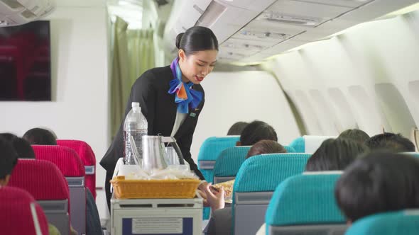 Beautiful Asian flight attendant or air hostess walking on aisle to check passenger in airplane. alt