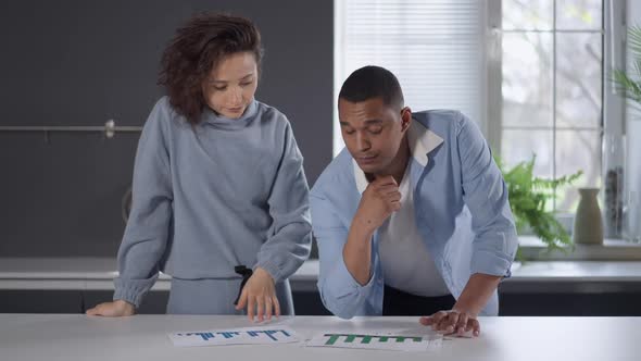 Serious Professional Interracial Couple of Analysts Examining Graphs in Home Office Looking at alt