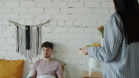 Caring Wife Bringing Tray with Food to Guy in Bed While Husband Watching TV Relaxing alt