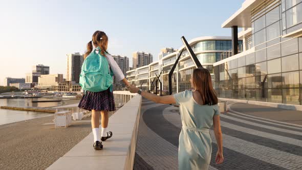 Young mother with little daughter in uniform going to school at morning