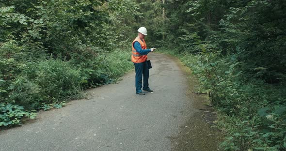Worker in Workwear and a Helmet on a Highway in the Forest