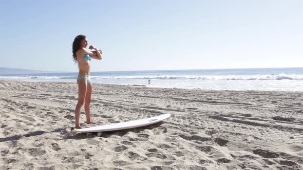 A young woman surfer stretching on the beach. alt