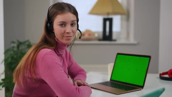 Charming Smart Young Woman in Headphones Posing with Green Screen Laptop in Home Office alt
