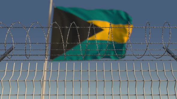 Flying Flag of Bahamas Behind Barbed Wire Fence alt