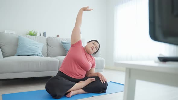 Asian large oversize women doing yoga workout in living room in house. alt