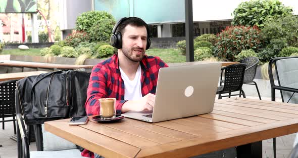 Cheerful businessman listening music in headphones while sitting in cafe near laptop. alt