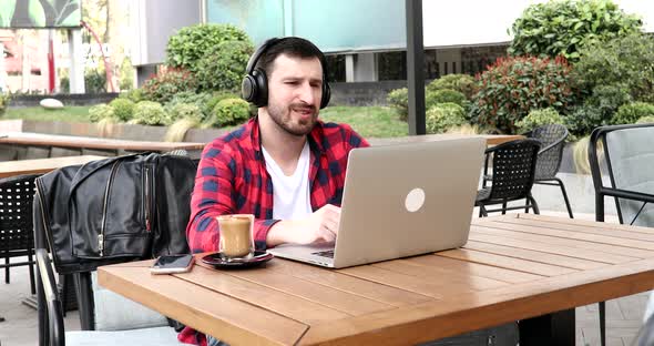 Cheerful businessman listening music in headphones while sitting in cafe near laptop.