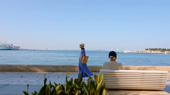 A young girl in a blue dress walking along the embankment in the city, video 6k alt