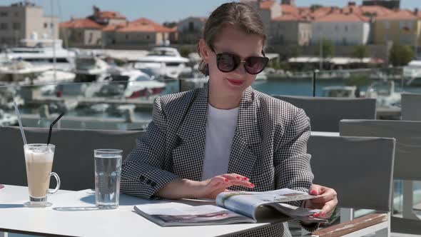 Young woman is sitting in the cafe and turns the pages of the magazine