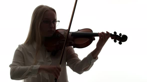 Blonde Woman in Glasses and White Blouse Plays with Bow and Fingers on Strings of the Violin in Dark alt