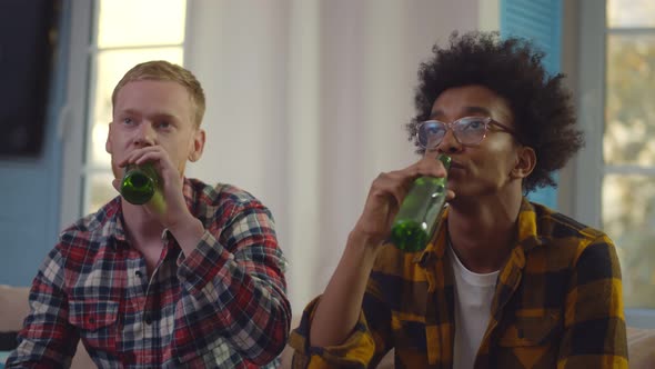 Young Diverse Friends Watching Tv and Drinking Beer at Home. alt