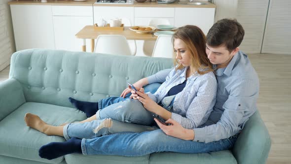 Guy and Girl Sit on Sofa Surfing Internet in Smartphones alt
