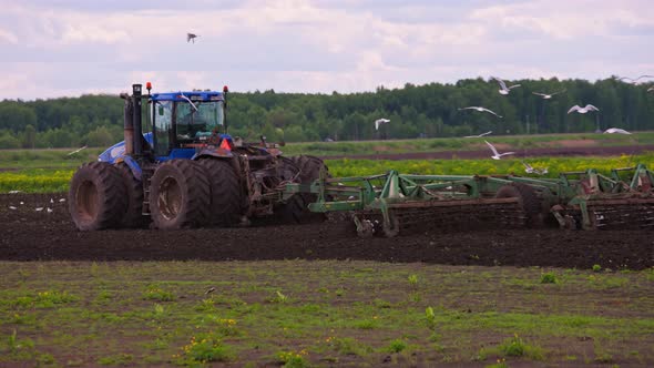 Blue Tractor with Double Wheels Pulling Disc Harrow with Roller Basket at Spring Day with Slow alt