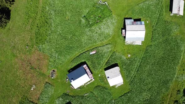 Drone Shot (facing down and rotating) of Chalets in Alpine Pastures under a Midday Sun alt