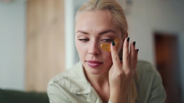 Concentrated blond woman sticking patches to eyes alt