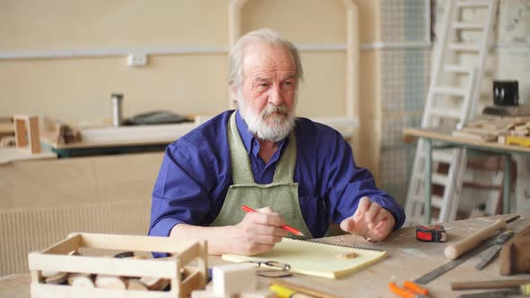 Old Journeyman with Many Wrinkles Sitting at the Desk with Tools. alt