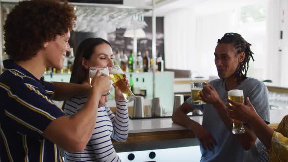 Diverse group of happy friends drinking beers and talking at a bar alt