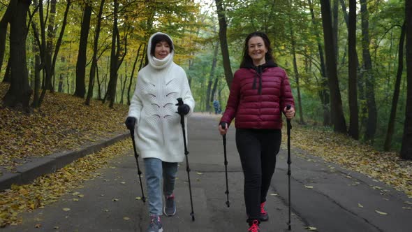 Dolly Shot Portrait of Two Confident Athletic Mature Women Strolling with Poles for Nordic Walking alt