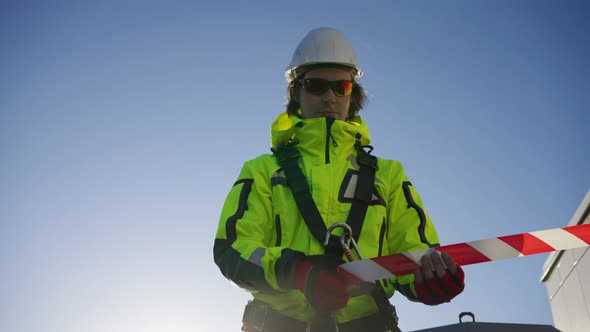 Industrial Climber in a White Helmet Encloses a Work Area with Signal Tape alt