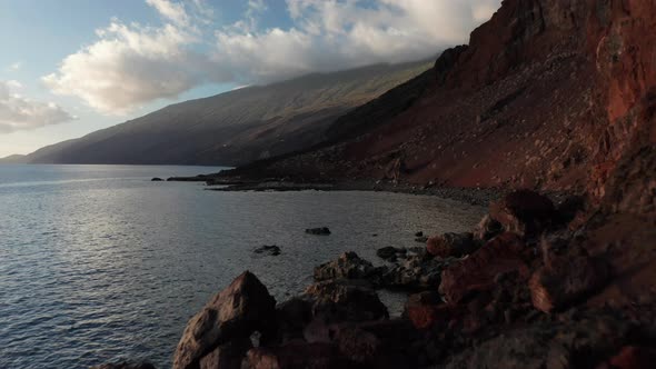 Aerial dolly close to cliff and boulders toward beach with black sand
