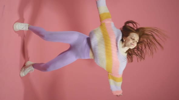 A Happy Laughing Young Woman in a Sweater and Leggings Poses Alone on a Pink Studio Background