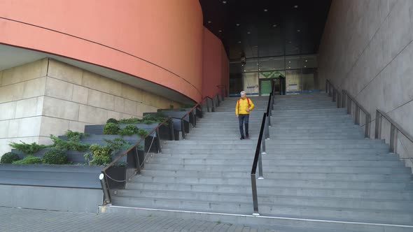 A Young Man Walks Down the High Stairs at the Large Building