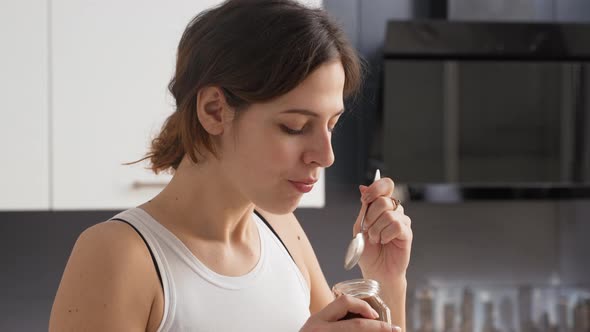 Hungry Charming Caucasian Female Eating with Pleasure Chocolate Spread on Kitchen alt