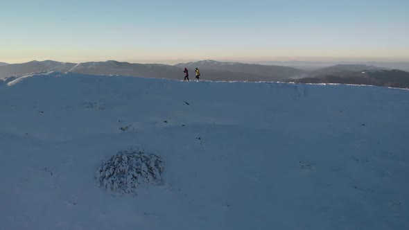 Drone Passing Couple of Hikers, Walking with Trekking Poles on Mountain Ridge in Winter
