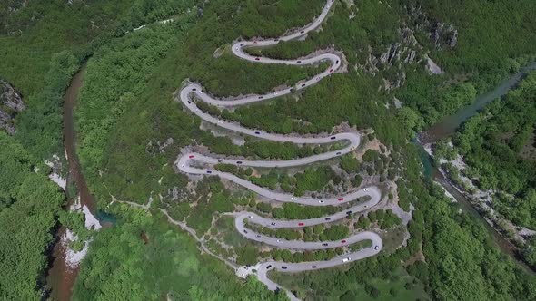 Drone shot of lots of race cars on curvy road in the mountain near Papingo, Greece. alt