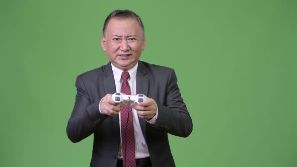 Mature Japanese Businessman Playing Games Against Green Background alt