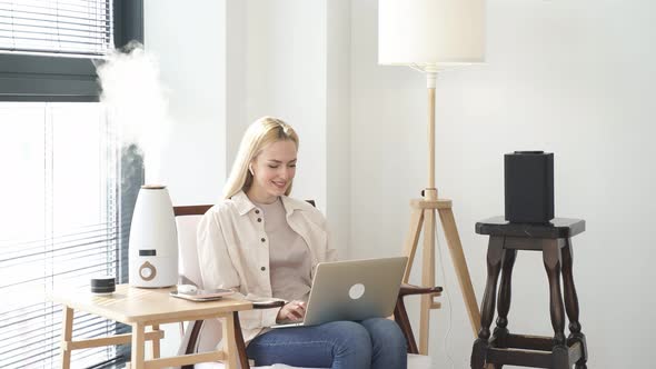 Adorable Caucasian Female Sit Working on Laptop with Purifier in Room in Smart House