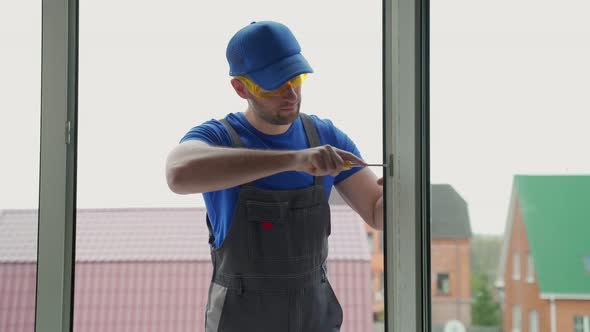 Worker Fixes Fastening for Window with Screwdriver Outside alt