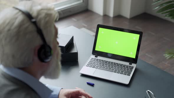 Elderly Mature Woman with Gray Hair and a Video Call on Her Laptop. Laptop with a Green Screen alt