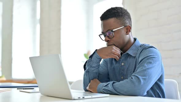Young African Man Thinking and Working on Laptop alt
