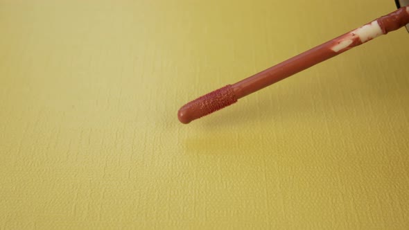 Brush Makes a Smear of Liquid Lipstick on Yellow Background