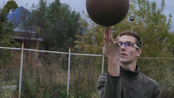 Caucasian Teenage Basketball Player with Glasses Rotates the Ball on the Finger