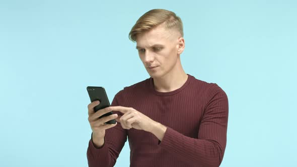 Handsome Blond Caucasian Man Casually Browsing on Smartphone Then Seeing Something and Staring at alt