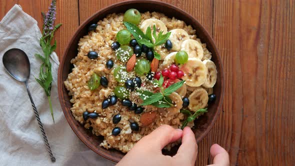 Wholegrain Oatmeal porridge with fresh berries, fruits nuts mint leaves sesame seeds in female hand alt