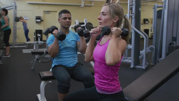 Woman lifting weights with trainer at gym