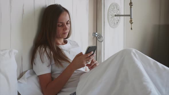 Young Woman Using Smartphone in Bedroom at Morning