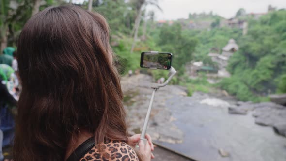 Girl with Long Hair in Leopard Dress Holds Gray Electronic Stabilizer with Phone Installed