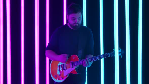 The Guitarist Enjoys His Electric Guitar Playing in a Dark Studio Surrounded By Bright Blue and Pink alt