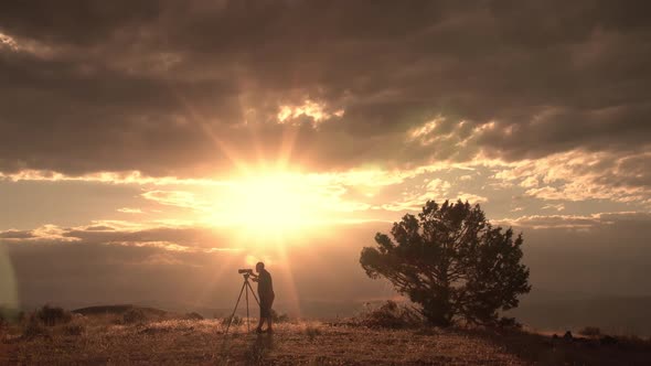 Photographer looking through sunset landscape on hill top alt