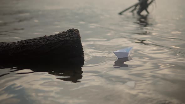 Paper Boat On River At Sunset. Origami Ship Sailing On Pond. Man Hand Launch Paper Boat On Water alt