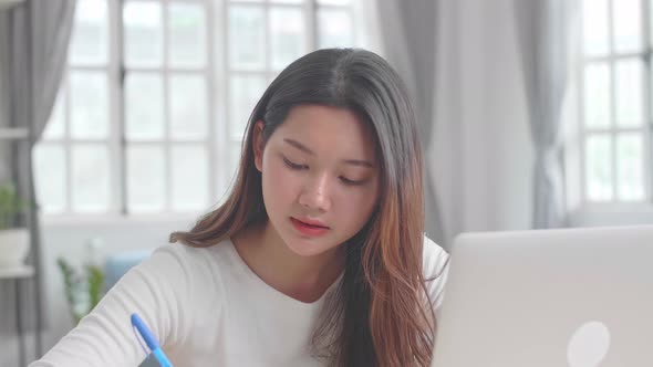 Asian Girl Using Laptop Computer And Writing On Notebook alt