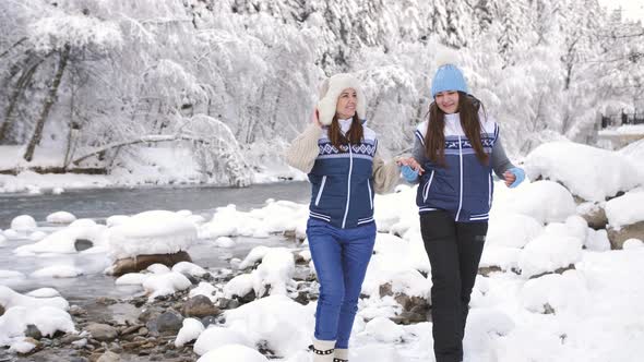 Two Girls in Love Walk Near the River in a Snowy Forest