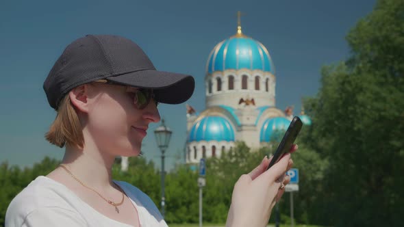 Young Woman Smiling Typing Text on Smartphone Orthodox Church in Background