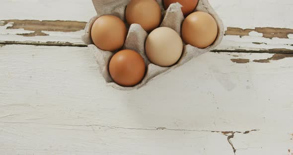 Video of overhead view of brown eggs in egg carton on rustic background alt