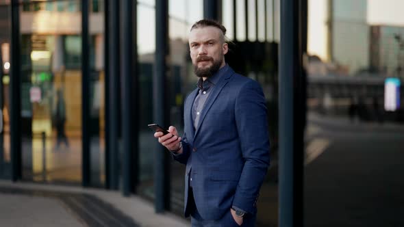 Portrait of a Mustachioed and Bearded Man in a Plaid Jacket and with a Phone in Hand at the Glass alt